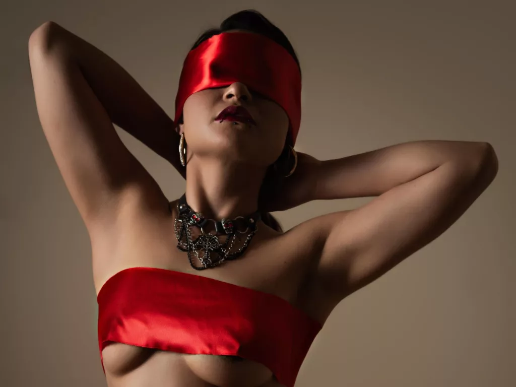 CassieJones blindfolded in red satin, black necklace, bare shoulders, soft lighting.