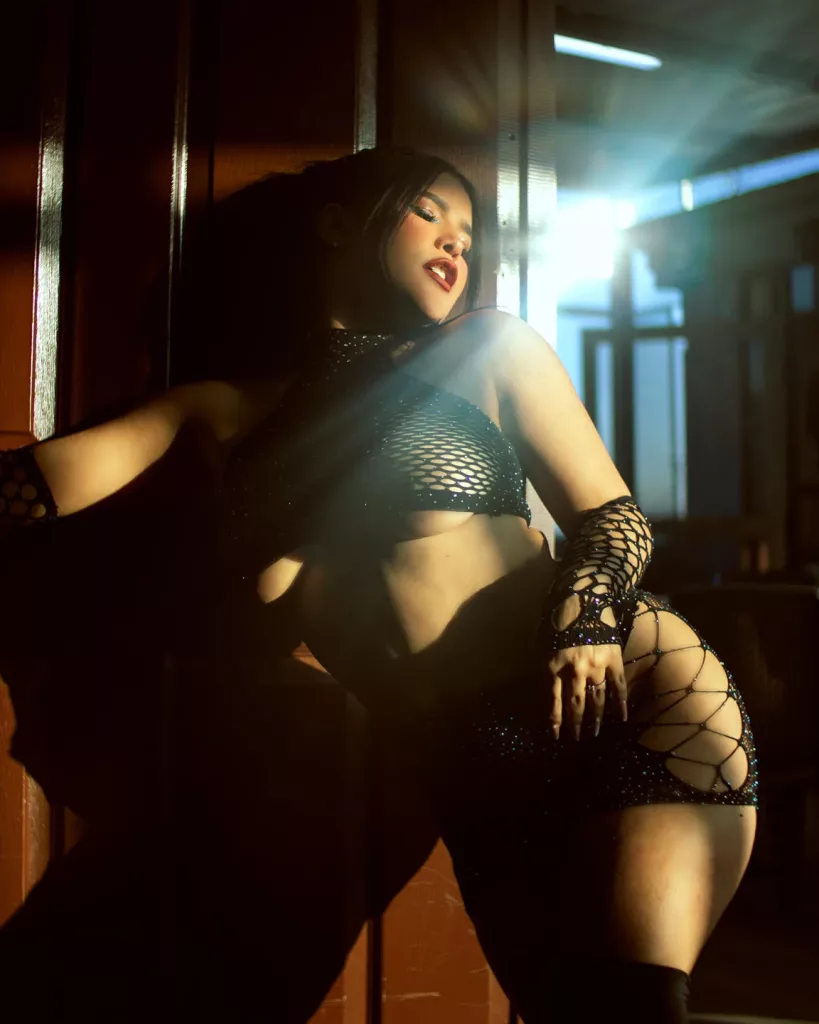  AvrillThomas takes a seductive photo in black mesh lingerie in a dark backlit room