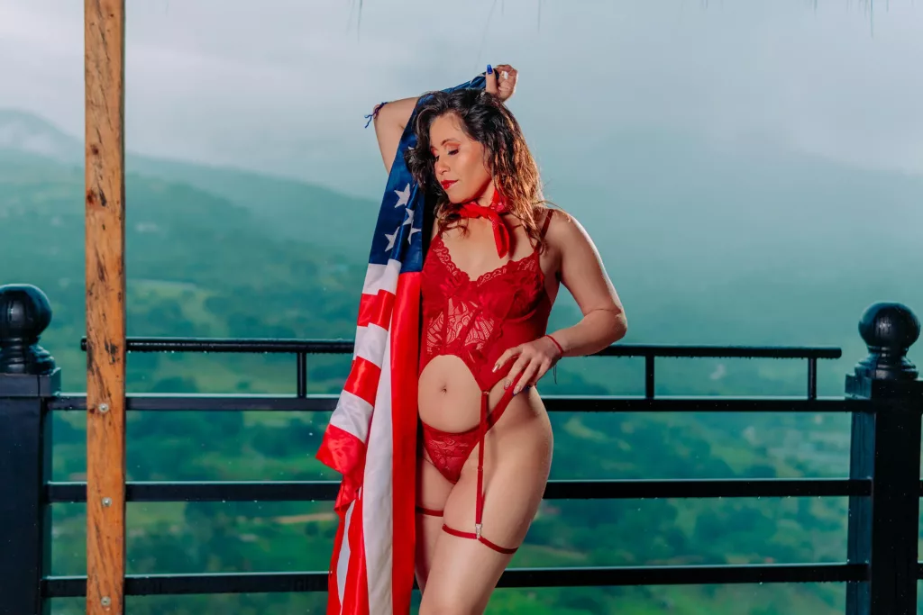 AnnyHotX poses in red lingerie with the American flag and mountainous background