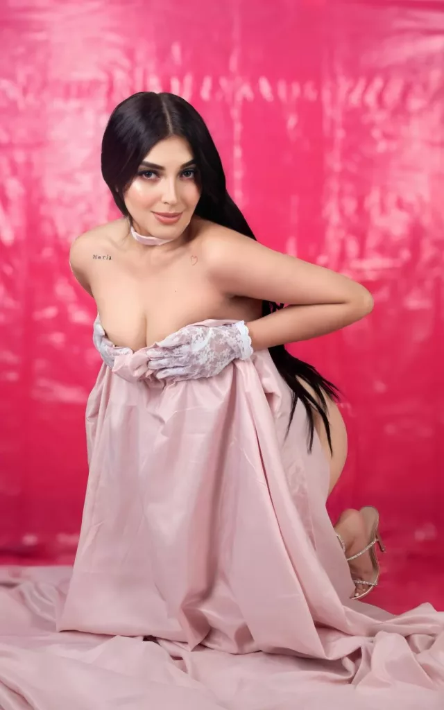 ArianaCortes take a picture in a studio with a red back ground hiding her nude body behind a curtain