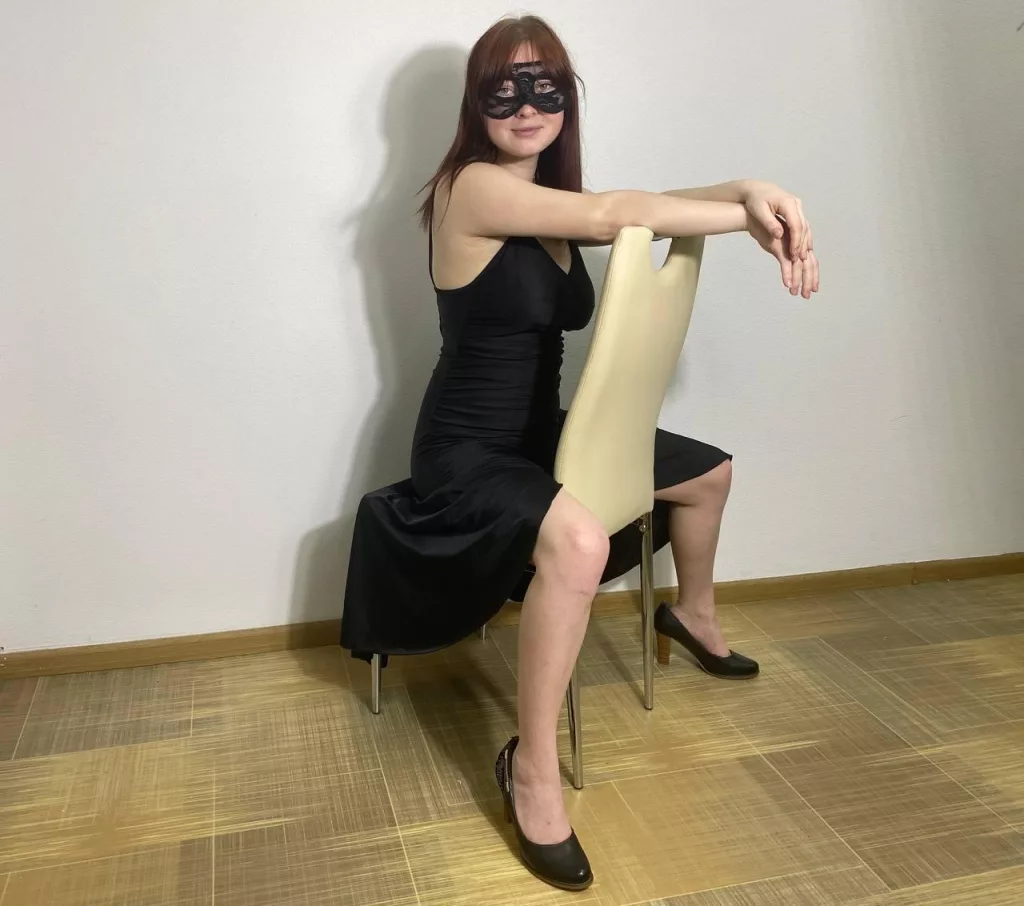 ErikaFin sits on her chair and is looking awesome in a black dress and mask