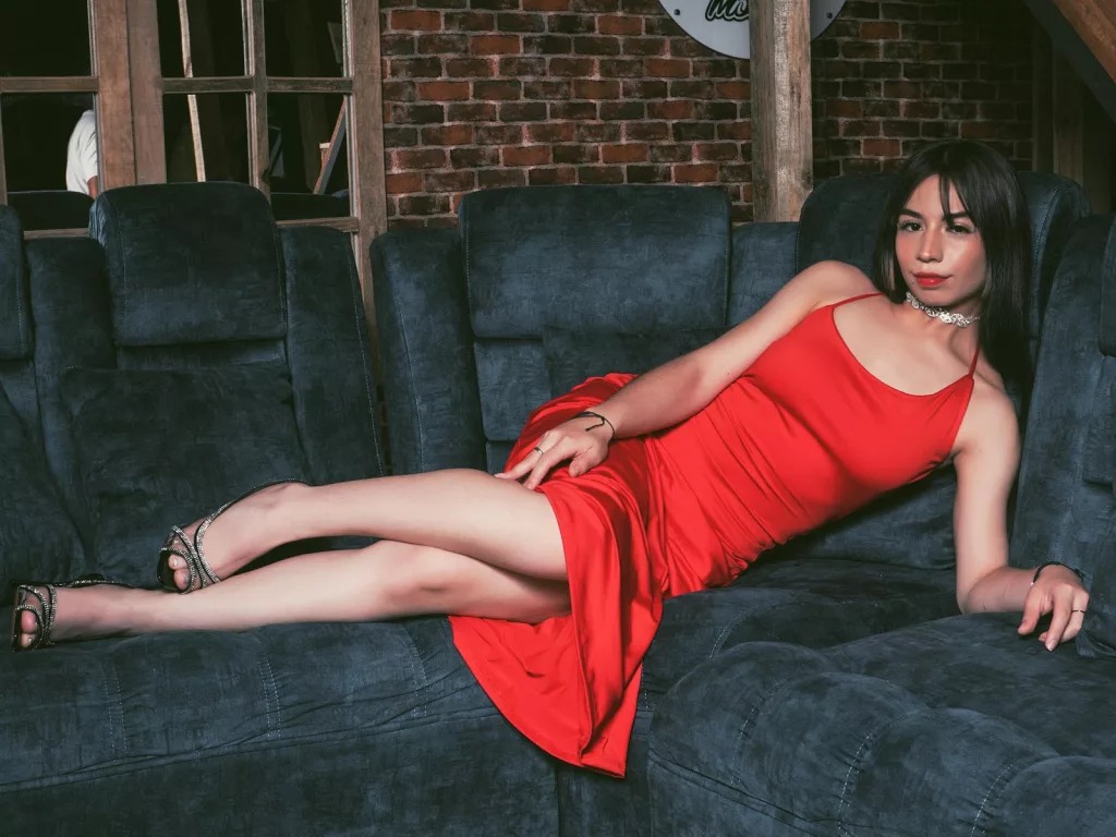 KatherinJohns in red dress, blue velvet couch, brick wall.