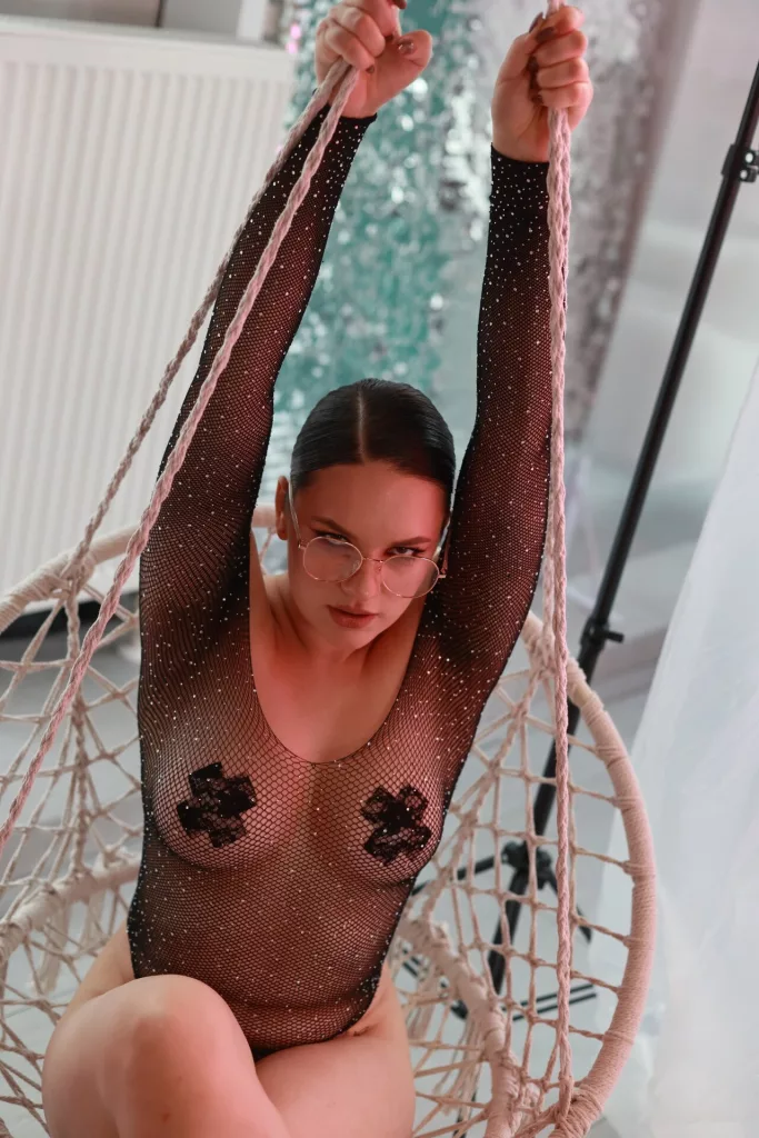 Dreia in sheer mesh leotard, hanging from white swing.