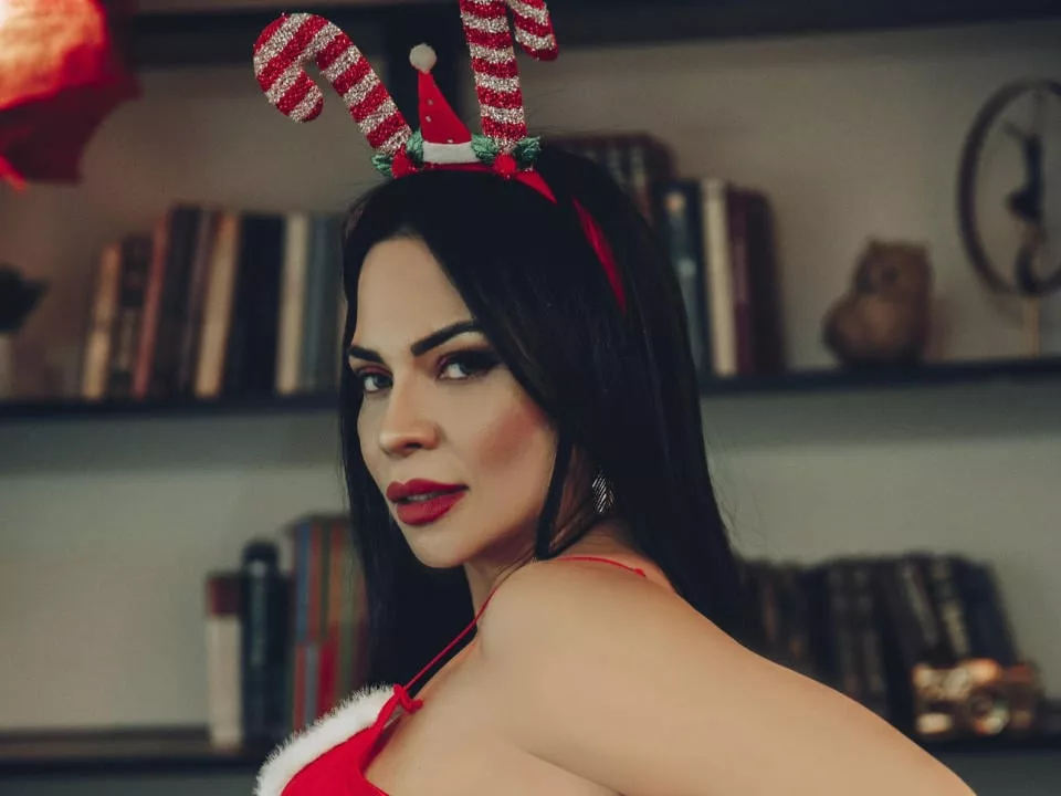 GemaHills in red Santa hat, top, and lipstick by bookshelf.