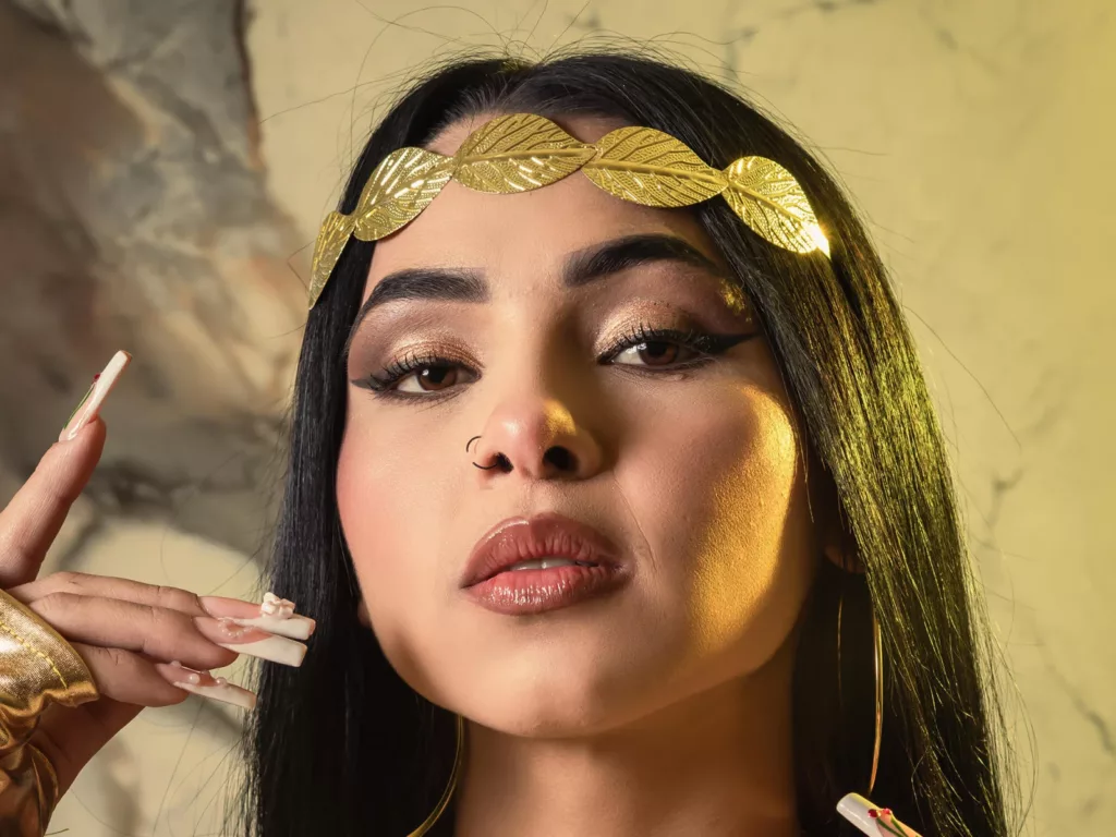 MistressAsshley holding BDSM leash, black outfit, confident pose, dark setting.