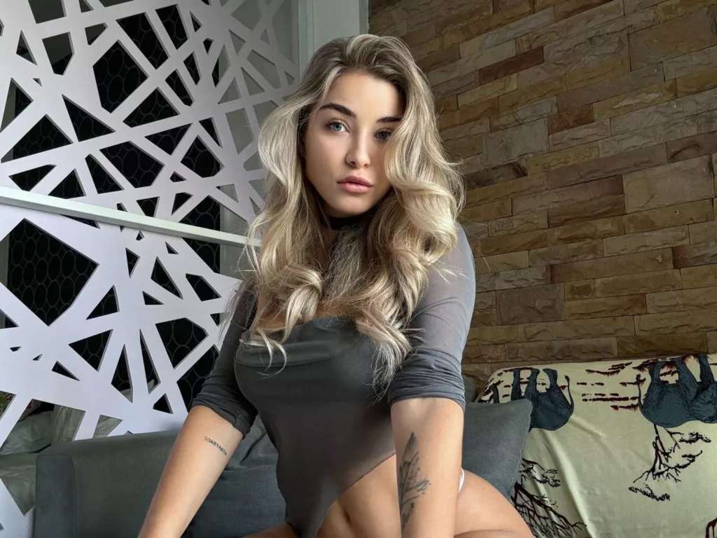 Ariemel in gray off-shoulder top, leaning on couch, flirty