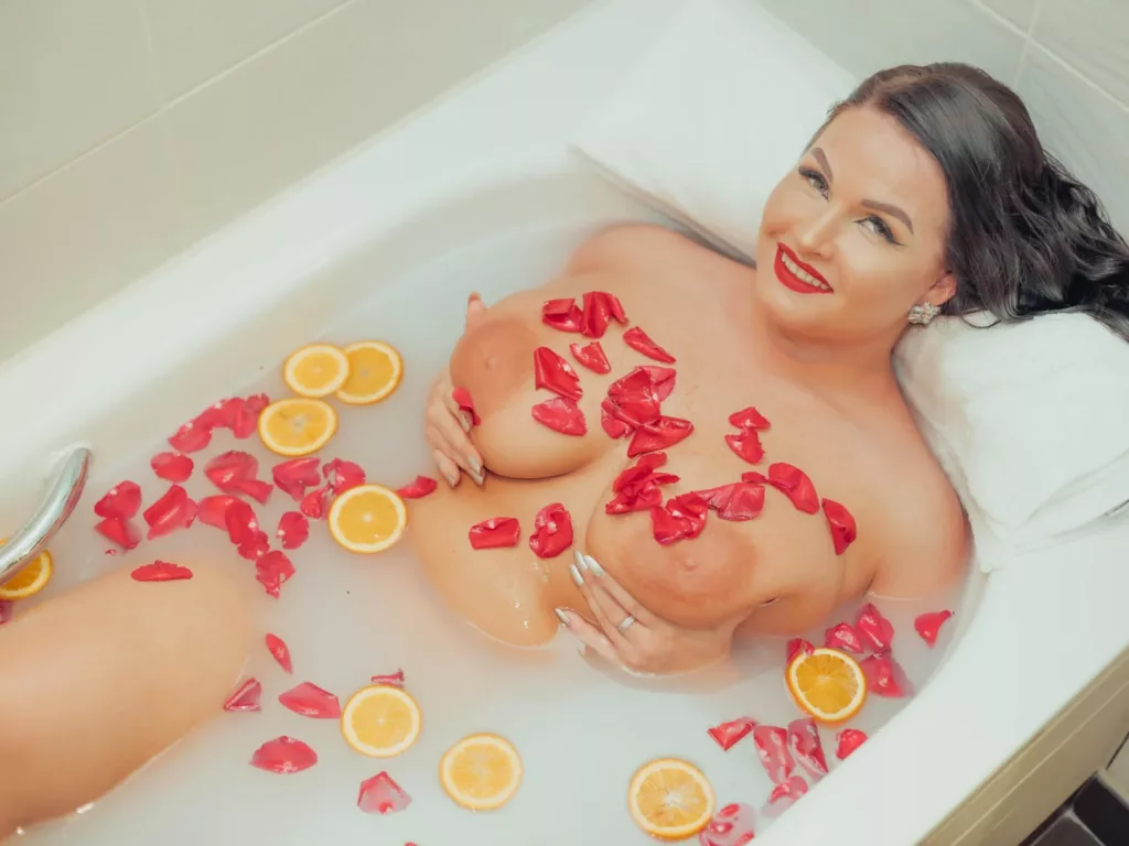 GeorgiaLerox naked in bathtub, covering large breasts with rose petals
