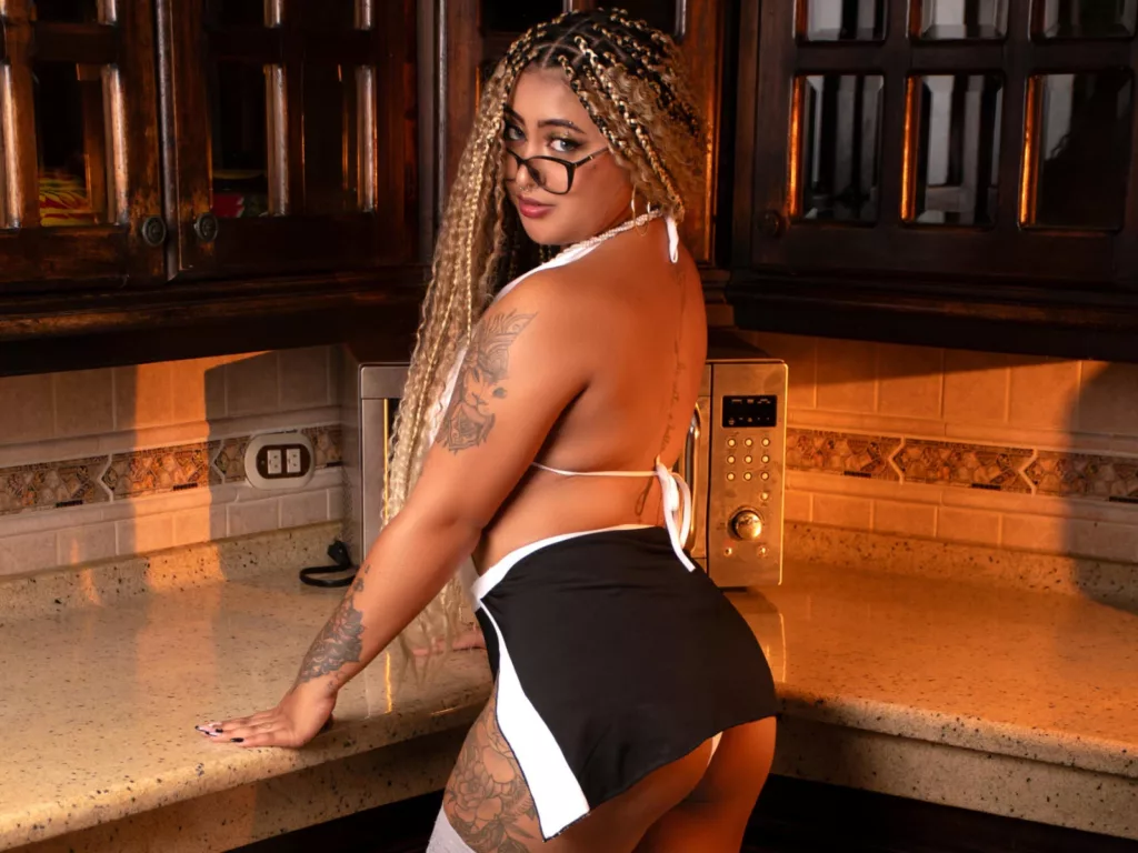 BBW ebony Latina LuisaCameron in white bikini top, leaning on kitchen counter.