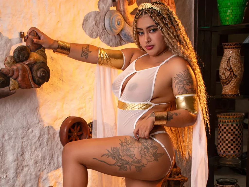 Ebony Latina XXX star LuisaCameron in sheer lace bodysuit, gold jewelry, and tattoos.