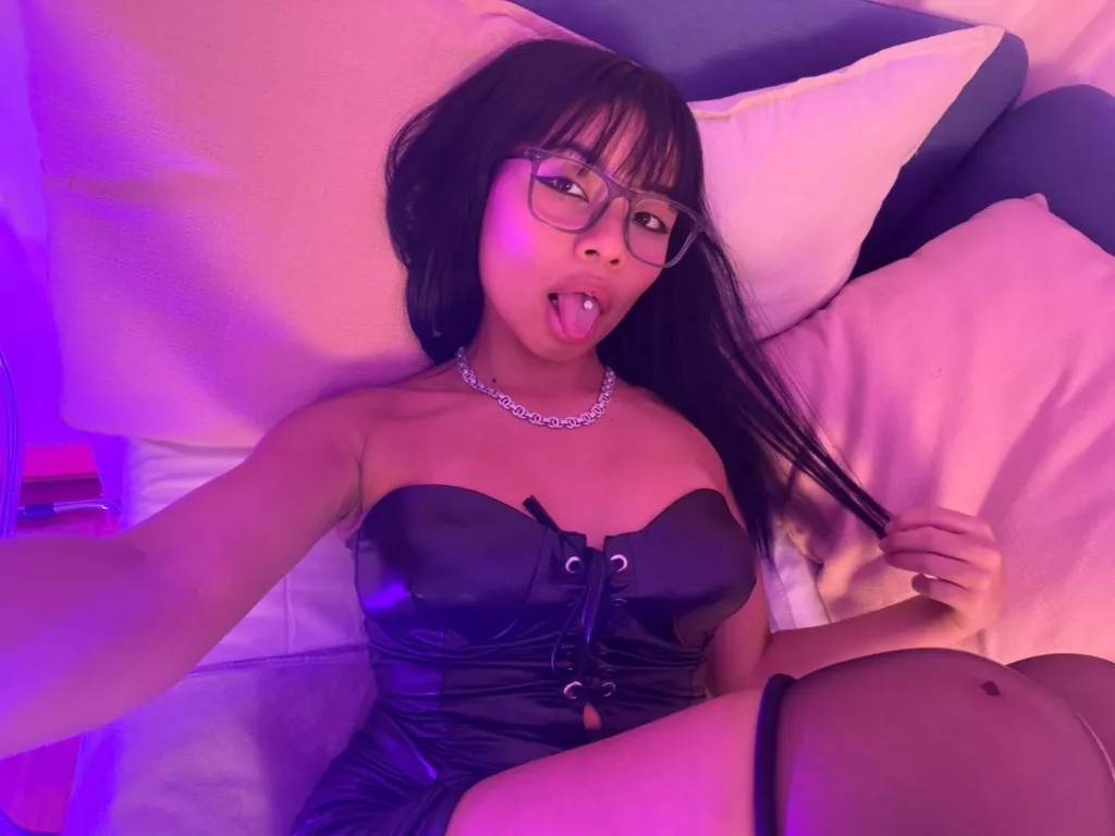 VannesaSaenz in black corset, playful tongue, neon-lit spoon cuddle position vibe.