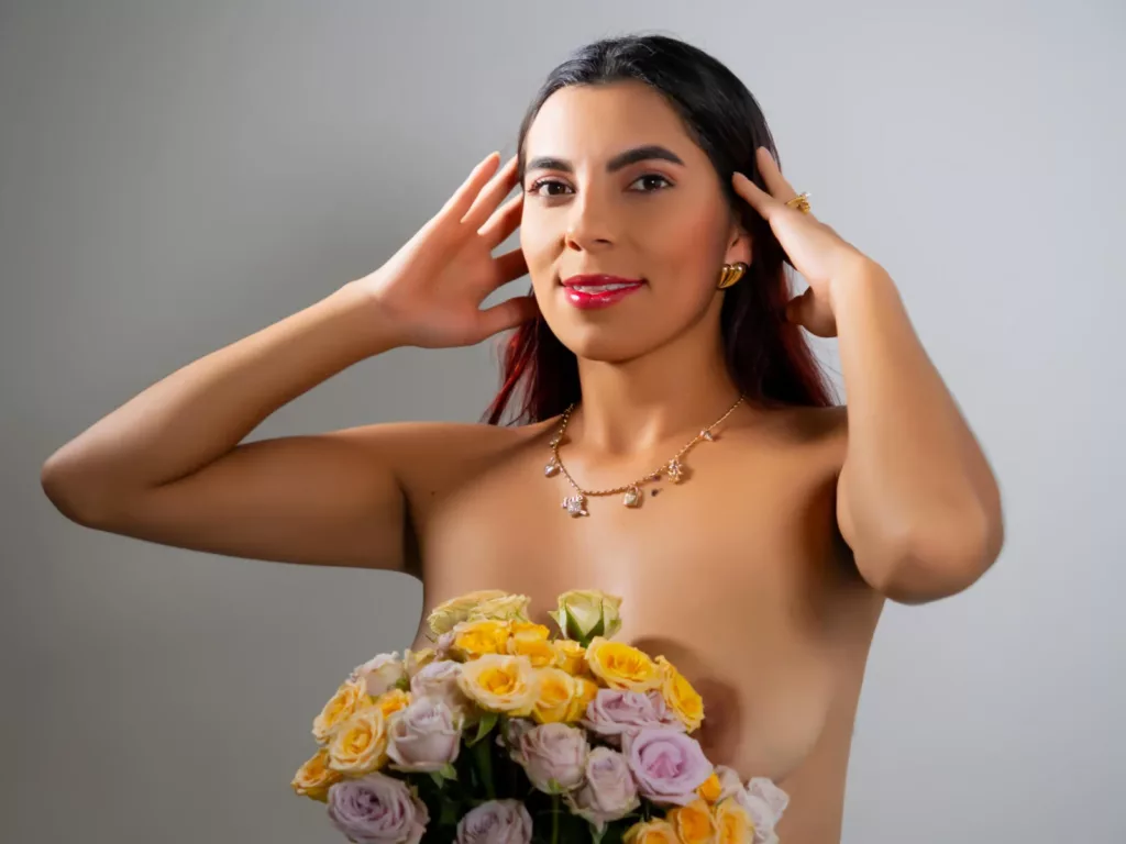 CarlaTorres, nude skinny Latina, clutches flowers, her gaze playful and inviting.