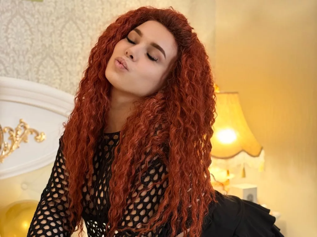 Niferttiti with long red curly hair and a black mesh top