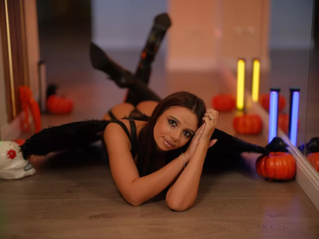 Aishabee as a dark angel, posing seductively in black lingerie amidst Halloween decor. nudist fetishism