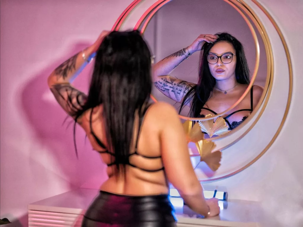 JustIzabel, the commanding BDSM Mistress, posing in a round mirror with tattoos on display