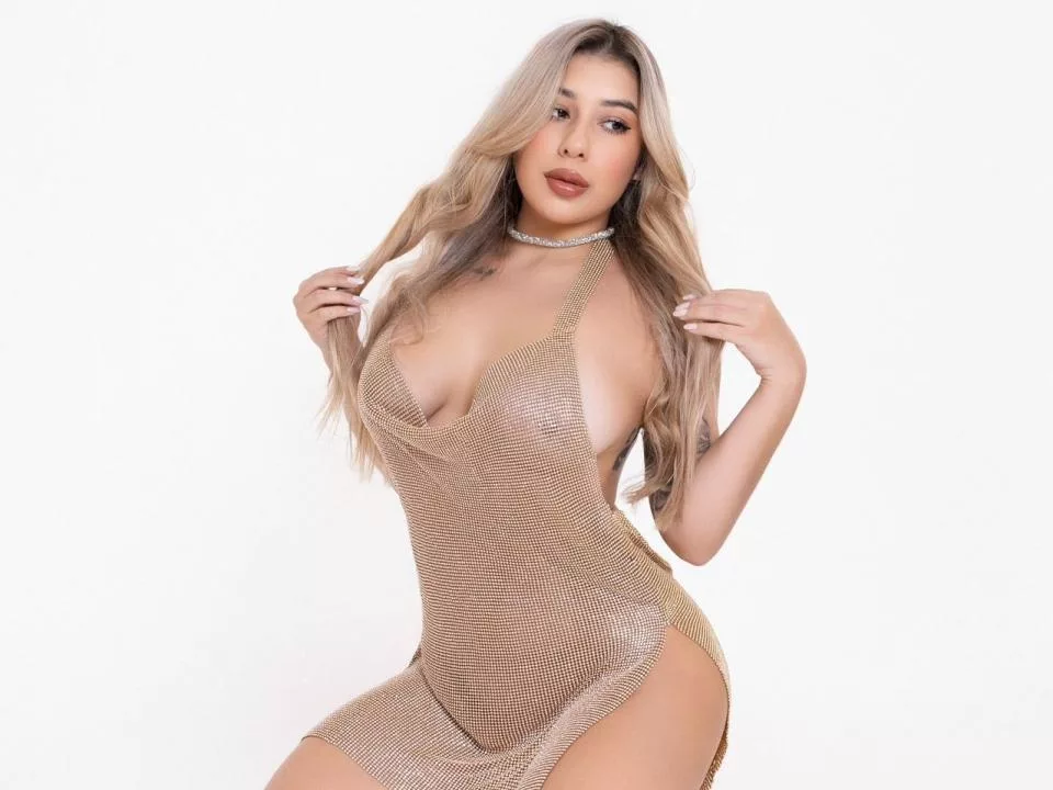 AgostinaNunier, blonde webcam model in a sheer mesh bodysuit with deep neckline and choker, confidently posing with one hand in her long blonde hair.